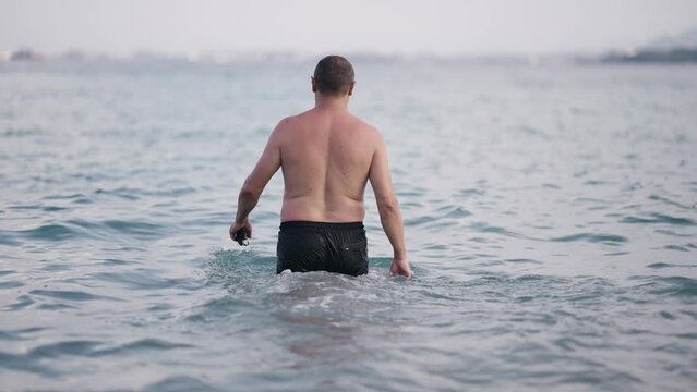 Handwome mand walk in sea water to swim wearing snorkeling googles in hand, slow motion. Cinematic selective focus footage