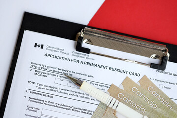 Application for permanent resident card on table with pen and canadian money close up