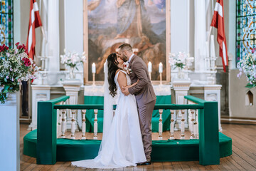 Valmiera, Latvia- July 28, 2024 - Bride and groom kissing at the altar, with witnesses by their side during a wedding ceremony...