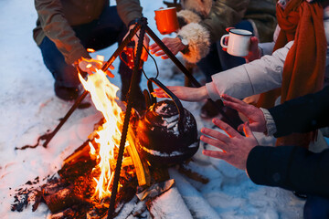 Group of friends gathering around bonfire in backyard, drinking tea and warming hands