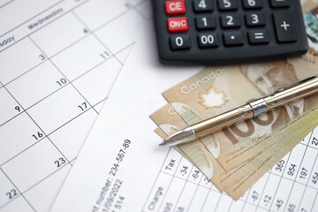 Fototapeta premium Many calculation results in schedules lies on table with canadian money bills, calculator and pen close up. Taxation and annual accountant paperwork in Canada