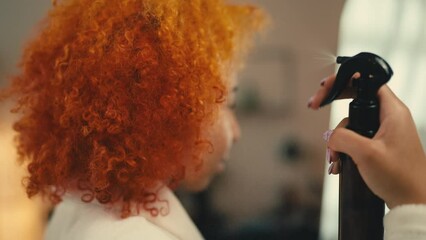 Young woman using smoothing spray on hair in front of mirror, haircare routine