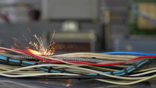 Flames, sparks, smoke between electrical cables, close up. Short circuit in the twisted wires from the electrical devices, fire hazard concept