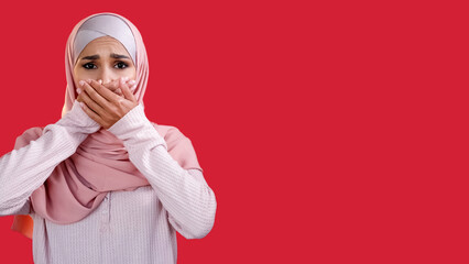 Fear anxiety. Shock stress. Disturbed scared worried woman in headscarf covering mouth with hands isolated on red empty space background. - obrazy, fototapety, plakaty