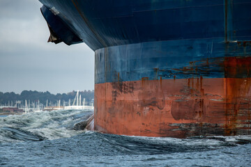 Big blue container ships bow with rusty anchors pushes a giant bow wave through the ocean.