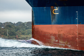 Big blue container ships bow with rusty anchors pushes a giant bow wave through the ocean.