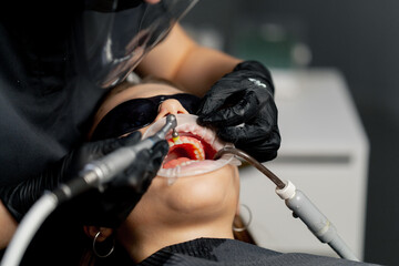 close up in a dental office female dentist in a cap is routinely cleaning the teeth of a young beautiful girl