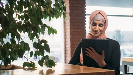 Online work. Remote job. Cheerful woman freelancer in hijab chatting online on digital tablet...