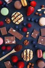 Macarons, chocolate, cookies, berries and various nuts on dark blue background. Top view.