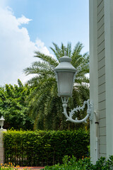 In the courtyard of a condominium, a white decorative lantern hangs on the side of the building. At night the electricity is turned on and it illuminates the area.