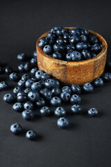 Fresh blueberries in a wooden bowl next to scattered blueberries on a dark background
