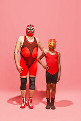 Two persons, middle-aged man and preteen boy, in superhero costumes posing against pink studio background. Concept of pop art, generation difference, costume festivals, competitions. Ad