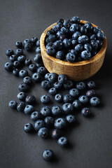 Fresh blueberries in a wooden bowl next to scattered blueberries on a dark background