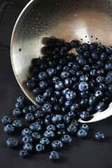 Fresh blueberries in a metal colander on a dark background