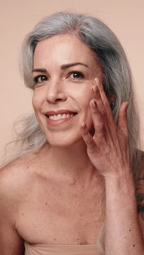 An elderly grey-haired woman posing confidently, showcasing her tattoo and elegance against a neutral background.