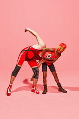Two athletes in wrestling poses, man and boy in red outfit with mask against pink studio background. Fight. Concept of pop art, generation difference, costume festivals, competitions. Ad