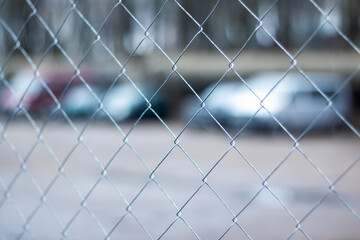 Closeup of metal chainlink fence with cars in background, electric blue tint