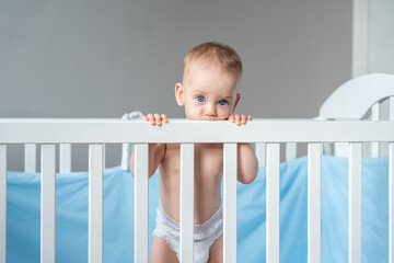 A baby in a diaper cutely bit the back of a wooden crib