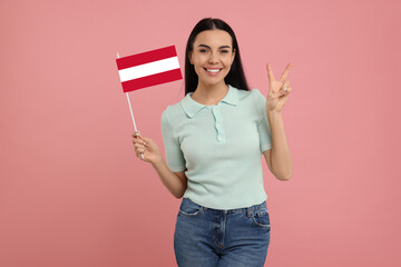 Happy young woman with flag of Austria showing V-sign on pink background