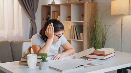Tired student. Study pressure. Education problem. Exhausted sleepy woman doing homework reading book sitting desk light room interior. - 787209100
