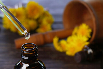 Dropper bottle of with tincture (water infusion, extract, perfume) and yellow dandelion flowers on wooden background . Side view. Space for text.            - obrazy, fototapety, plakaty