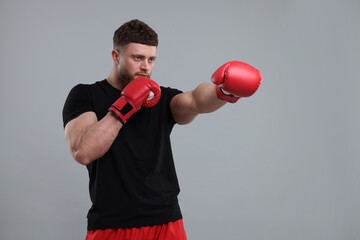 Man in boxing gloves fighting on grey background - obrazy, fototapety, plakaty