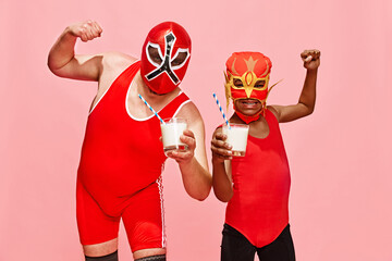 Two masked wrestlers in red, flexing muscles and holding milkshakes against pink studio background. Concept of pop art, generation difference, costume festivals, competitions. Ad