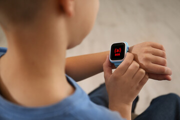 Little boy using SOS function on smartwatch indoors, closeup