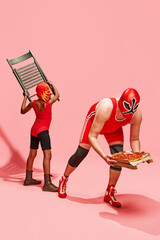 Man in wrestling clothes, athlete trying to steal box of pizza from his partner so that he can eat it all alone against pink background. Concept of pop art, healthy lifestyle, competitions. Ad