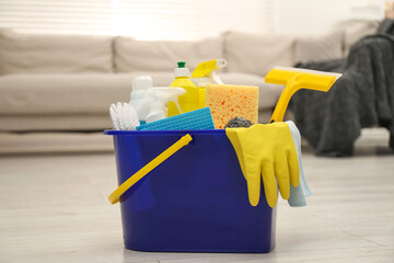 Different cleaning supplies in bucket on floor at home - obrazy, fototapety, plakaty