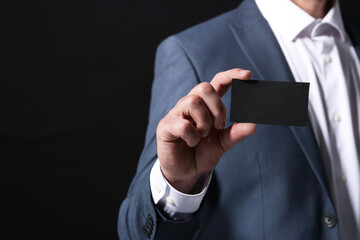 Businessman holding blank business card on black background, closeup. Space for text