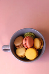 Purple cup filled with pastel macarons on pink background. Selective focus.