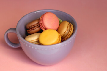 Purple cup filled with pastel macarons on pink background. Selective focus.