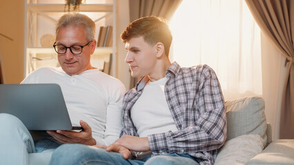 Shopping online. Family generation. Internet leisure. Happy father and son surfing on laptop together home living room.