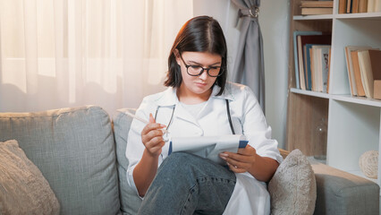 Working doctor. Medical report. Busy woman physician filling clinical patient form writing prescription on clipboard on couch at hospital. - 787216938