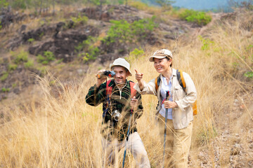 active senior couple hiking together on summer time,a mature male looking into binoculars and smiling,concept of elderly pensioner lifestyle,family relationship,activity,travel,adventure in nature