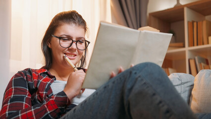 Studying student. Homework joy. Smiling woman enjoying book exam learning happy with high school lesson on couch at home.