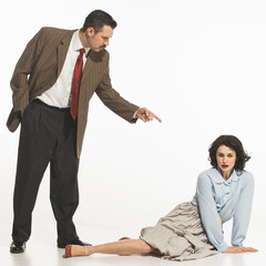 Man in suit pointing at seated woman on the floor, suggesting confrontation, dispute. Family...