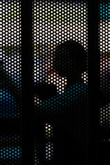 Holes.  The silhouette of a woman is seen through holes in a mesh fence.