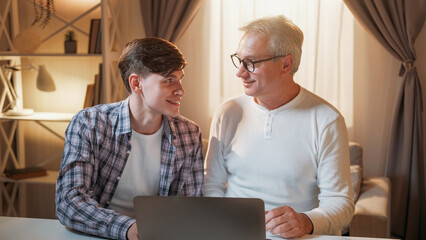 Family shopping. Online assistance. Digital life. Happy son and father making purchase using laptop sitting light home interior.