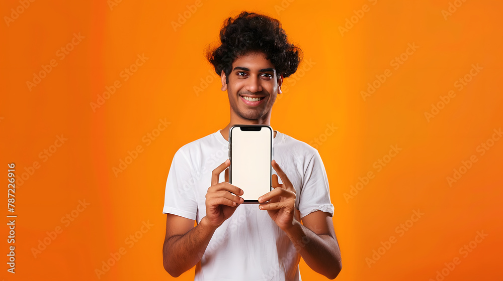 Poster positive curlyhaired happy indian guy in white tshirt holds smartphone with mockup blank white scree