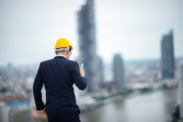 A Portrait of Industry factory engineer, architect or inspector in Safety Uniform is standing on rooftop of factory or building. Smart, professional, expertise and Confidence factory manager looking.