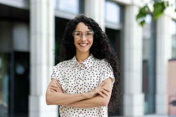 Professional and confident Hispanic woman with curly hair, wearing glasses and a polka dot shirt,...
