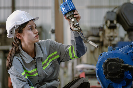 Industrial engineer woman working on robot arm maintenance in futuristic technology factory. Technician checking robotic automated welding torch machine to control electronic welder innovation process