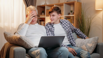Online connection. Family relationship. Happy inspired father and son discussing information on laptop sitting sofa at room interior.