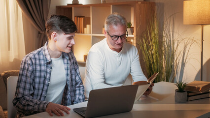 Homework together. Father help. Family leisure. Happy dad discussing lesson with joyful son at laptop sitting desk home interior.
