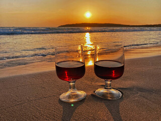 Two glasses of red wine stand on the sand on the beach. Scenic sunset over the sea. The sun goes below the horizon - Sardinia, Porto Pino