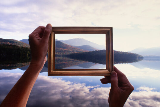 Woman's hands holding picture frame up to calm Lake Placid and hills