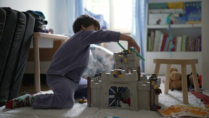 Small boy playing in bedroom with toy castle at home wearing pajamas. Child engrossed in...
