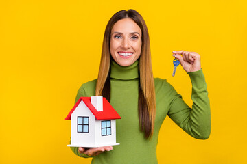 Fototapeta na wymiar Photo of cheerful satisfied girl hold little house demonstrate key isolated on yellow color background